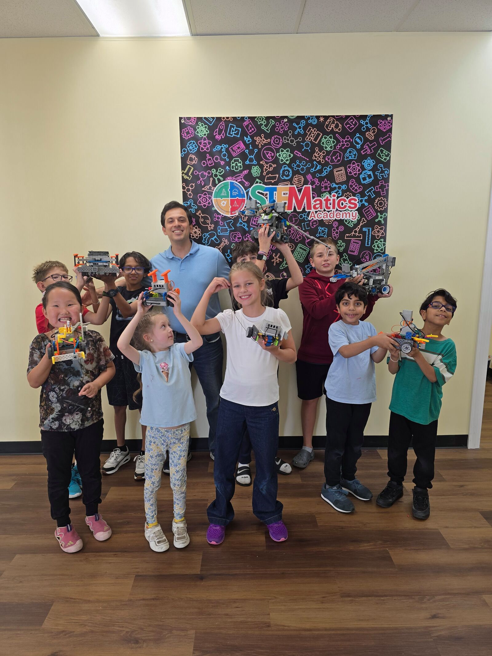 Camp students and an instructor holding up the robots they built in front of the STEMatics Academy banner