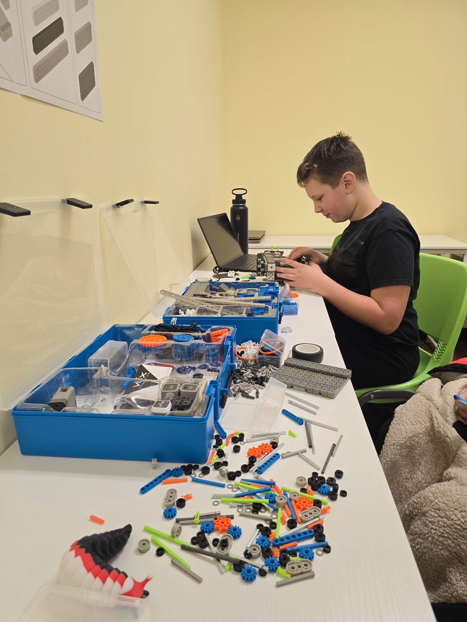 A camper assembling a robot beside an open robotics kit