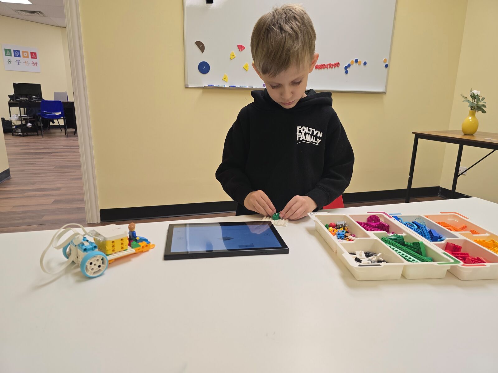 A student building a brick-based robot with instructions on a tablet
